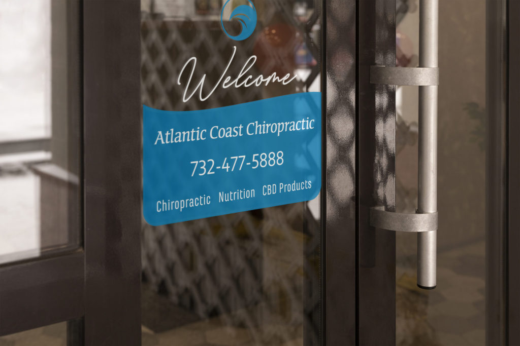 The Atlantic Coast Chiropractic logo is printed on a glass door above the word 'Welcome' and a blue wave area with business name, phone number, and services offered. The logo features a blue stylized wave inside a circle.