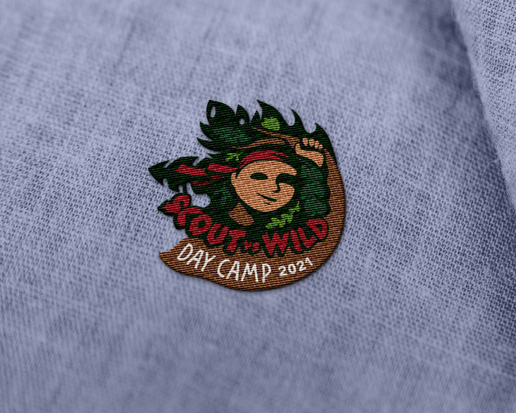 a green and brown embroidered patch featuring the silhouette of a boy's face with a red bandana, surrounded by leaves and the words "Scout vs. Wild - Day Camp 2021"
