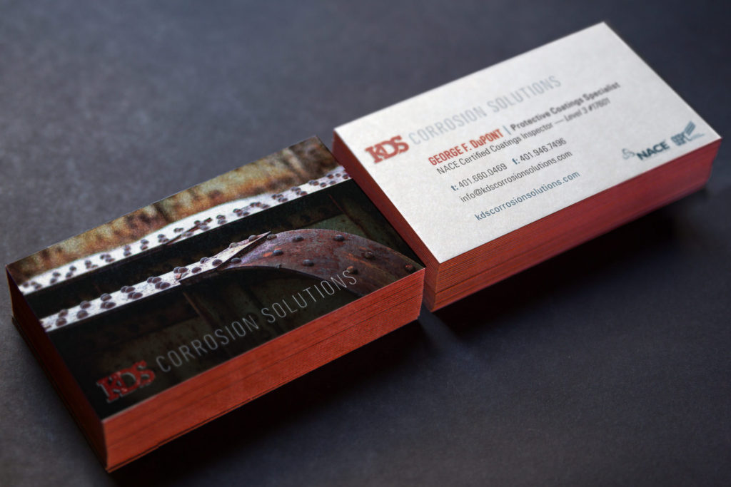 two stacks of cards with rust red edge painting show both sides of a business card design. the front side features a textural image of rusted steel sturctual comonents and the back features the business logo and contact information on a white background.