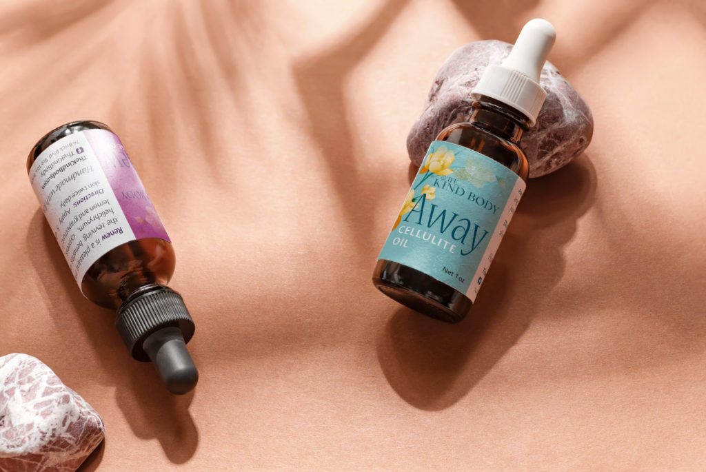 Two dark glass dropper bottles are laid out on a terracotta colored background with abstract shadowing. The bottle on the right is propped up on a small rock and wrapped with a teal and yellow floral product label. The bottle on the left sits upside down with the white ingredient side of the label facing up.